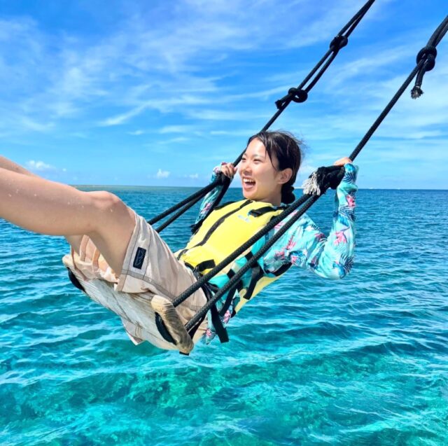 青い海と空を背景に海上ブランコではしゃぐ女性