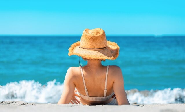 美しい沖縄の海を眺める麦わら帽子を被った女性