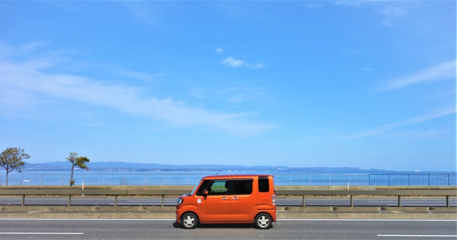 海沿いの道路を走るオレンジ色の車と青い海の風景